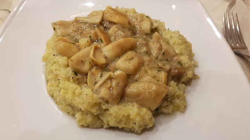 Creamy yellow polenta topped with glossy browned mushroom pieces and herbs on a white plate