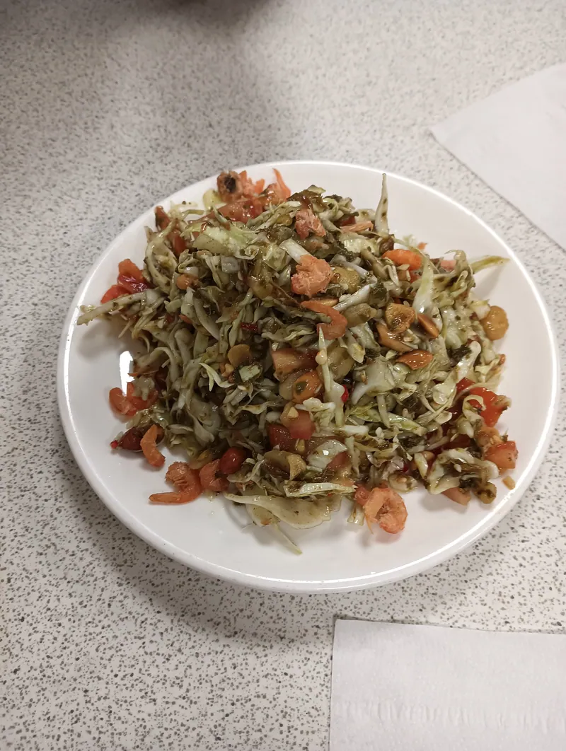 Burmese-style tea leaf salad with shredded cabbage, tomatoes, peanuts, seeds and dried shrimp on a white plate