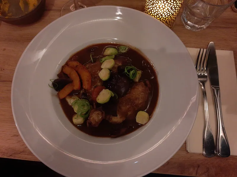 Chicken pieces and mushrooms in a dark red-wine sauce served in a wide white bowl