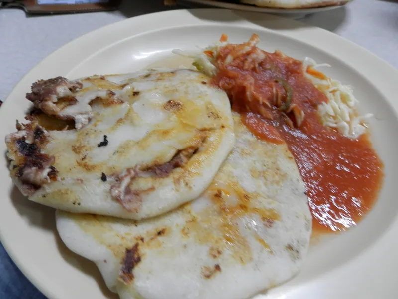 Three thick Salvadoran-style pupusas with browned griddle marks, refried bean and cheese filling, curtido and red salsa