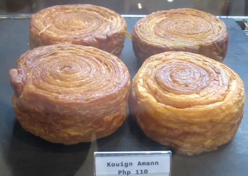 Four golden individual kouign-amann pastries showing crisp caramelized rims and distinct spiral butter layers