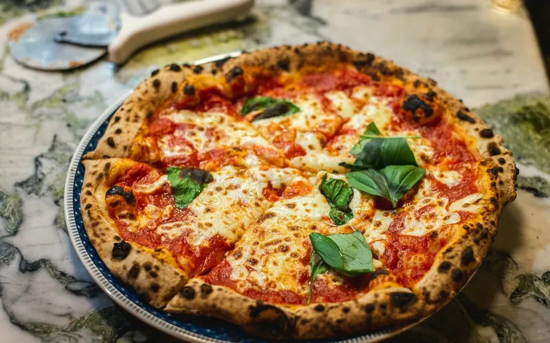 Round Margherita pizza with a blistered golden crust, red tomato sauce, melted mozzarella and fresh green basil leaves