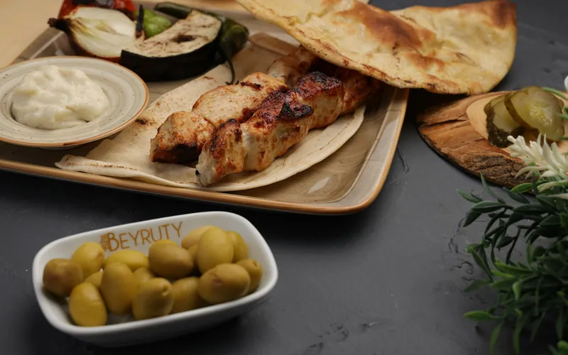 Char-grilled chicken shish tawook skewers on warm pita with white garlic yogurt, cucumber pickles, green olives, grilled eggplant, onion, tomato, and green pepper