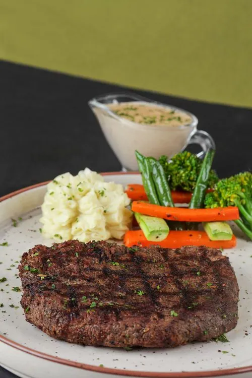 Seared ribeye with creamy mashed potatoes, green beans, carrots, and herb sauce