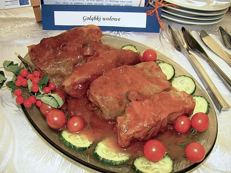 Polish gołąbki cabbage rolls filled with beef and rice and covered in red tomato sauce on a platter with fresh vegetables