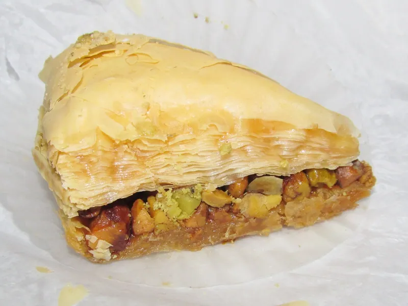 Close-up of a square pistachio baklava showing many crisp golden phyllo layers and a thick filling of chopped green pistachios