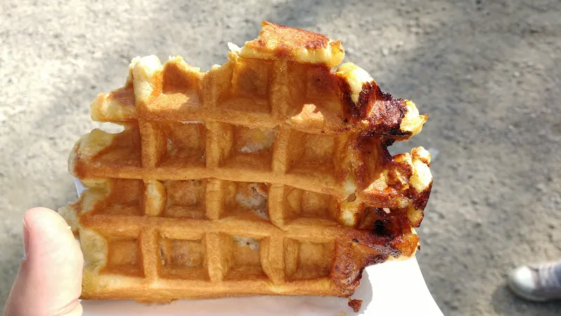 Close-up of a handheld Belgian Liège waffle with a thick golden grid and deeply caramelized pearl-sugar edges