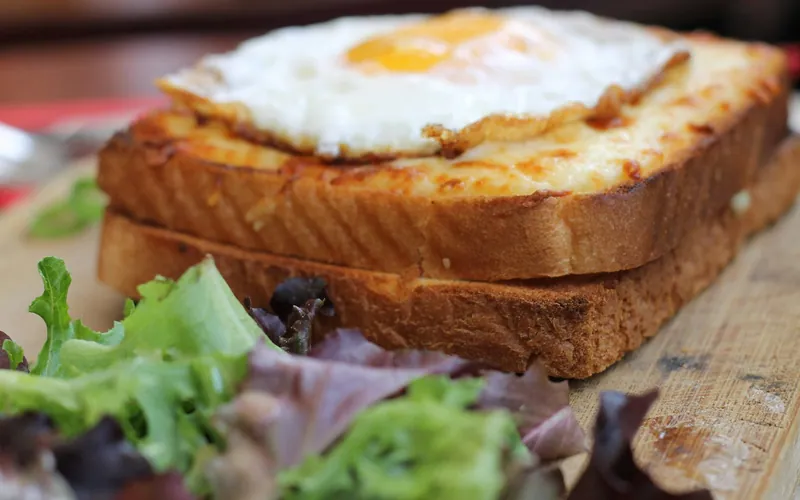 Golden croque madame sandwich with melted Gruyère béchamel and a sunny fried egg on top, served beside mixed green salad