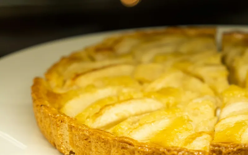 Golden round pear tart with overlapping pear slices in almond filling and a tall fluted pastry crust on a white plate