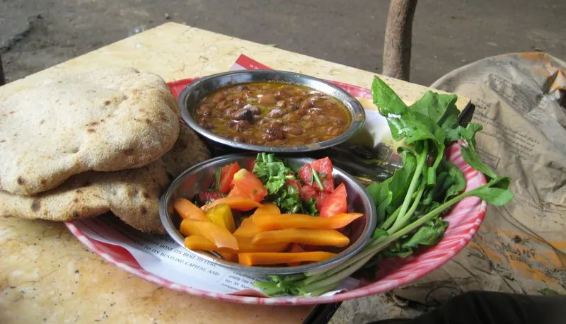Egyptian-style ful medames breakfast platter with a bowl of fava beans, pita breads, pickled vegetables, tomato salad and fresh rocket leaves