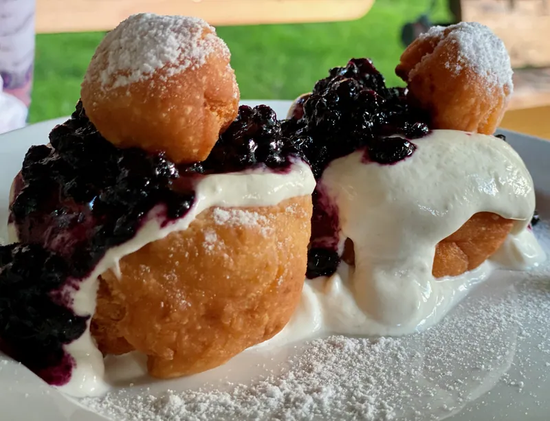 Two Romanian papanași cheese doughnuts topped with sour cream, dark blueberry preserves and small doughnut rounds