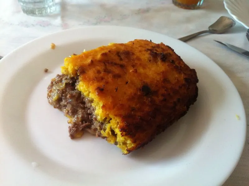 Cut serving of Chilean-style pastel de choclo showing a browned golden corn topping over a juicy beef filling