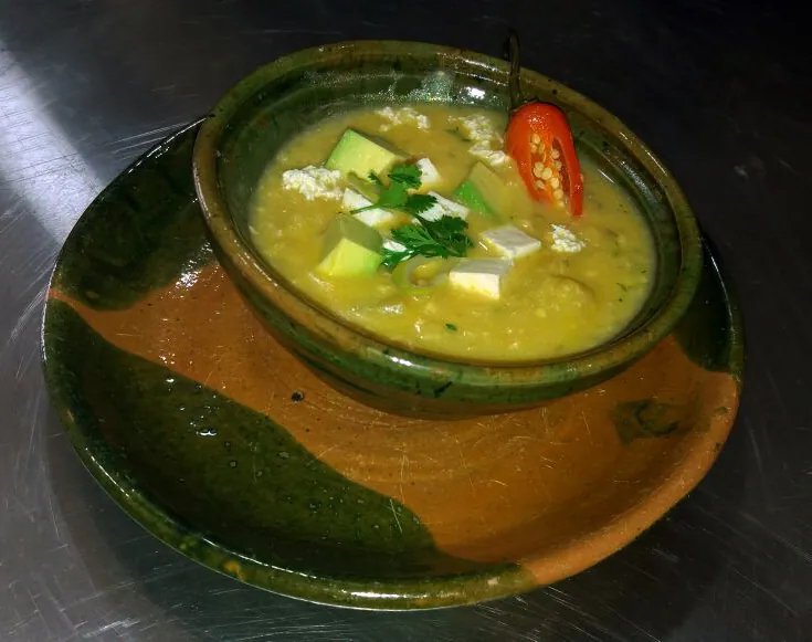 Golden Ecuadorian locro de queso potato soup topped with avocado, white cheese and cilantro in a rustic bowl
