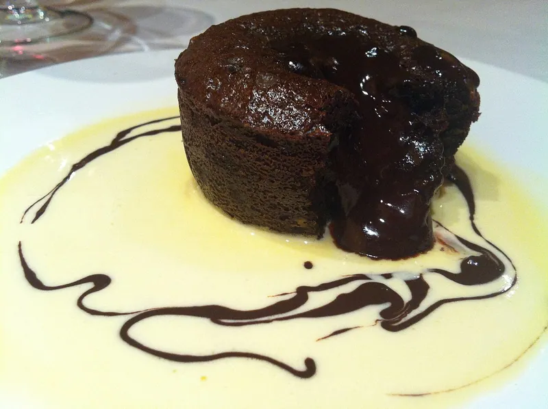 Individual dark chocolate molten cake with a glossy flowing center set in pale vanilla crème anglaise with thin chocolate swirls