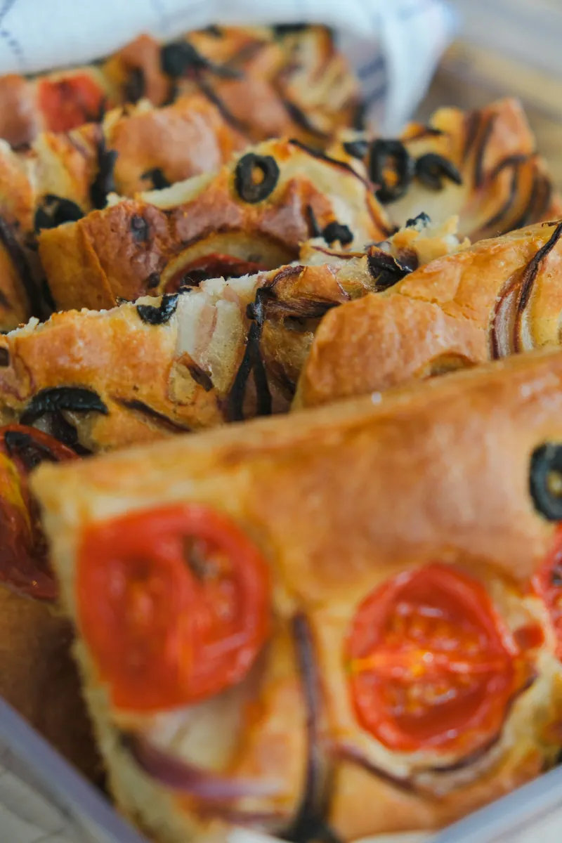 Cut focaccia pieces topped with halved tomatoes, black olive rings and thin red onion