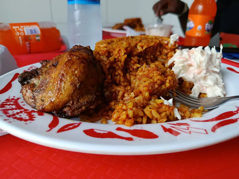 Plate of red Nigerian jollof rice with crisp fried chicken and creamy coleslaw