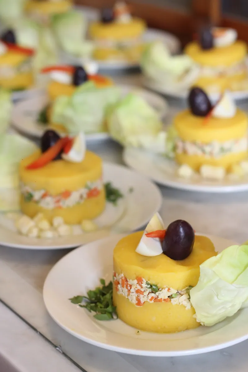 Individual Peruvian causa rellena stacks with bright yellow potato layers, creamy tuna filling, red pepper, lettuce and black-olive garnish