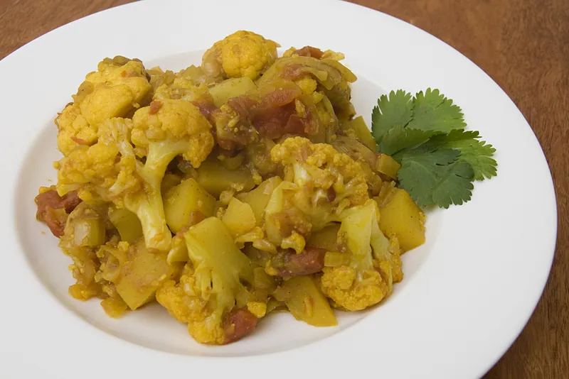 Golden aloo gobi with cauliflower florets, potato cubes, tomatoes and fresh cilantro on a white plate