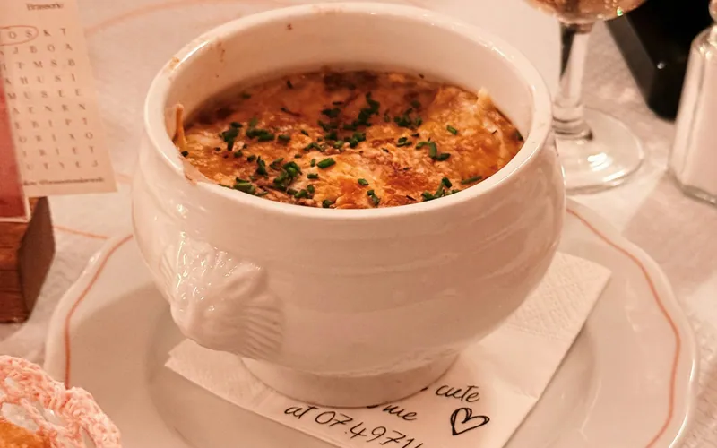 White handled crock of French onion soup covered with bubbling browned cheese and finished with chopped chives
