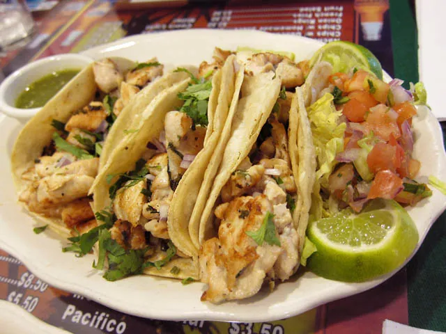 Chicken tacos in soft tortillas with green salsa, onion, cilantro, lime, rice and black beans