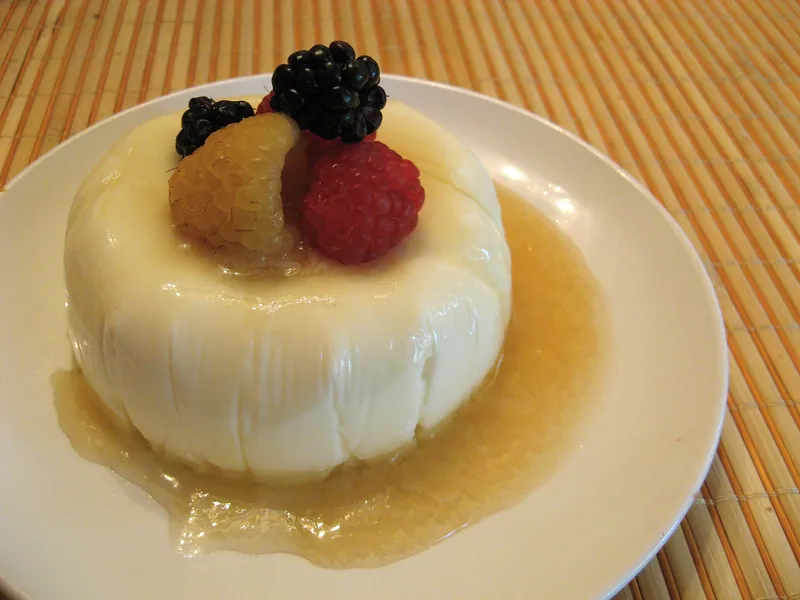 Fluted white panna cotta topped with golden and red raspberries and blackberries in a clear honey drizzle