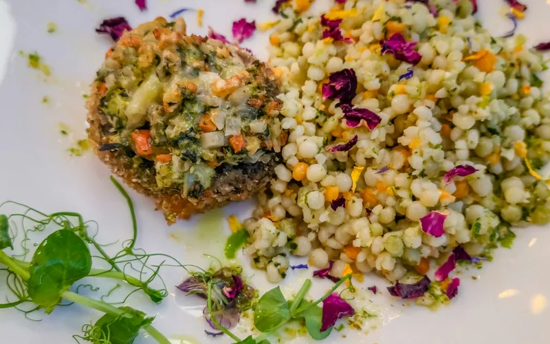 Spinach-stuffed portobello beside pearl couscous with edible petals and pea shoots on a white plate