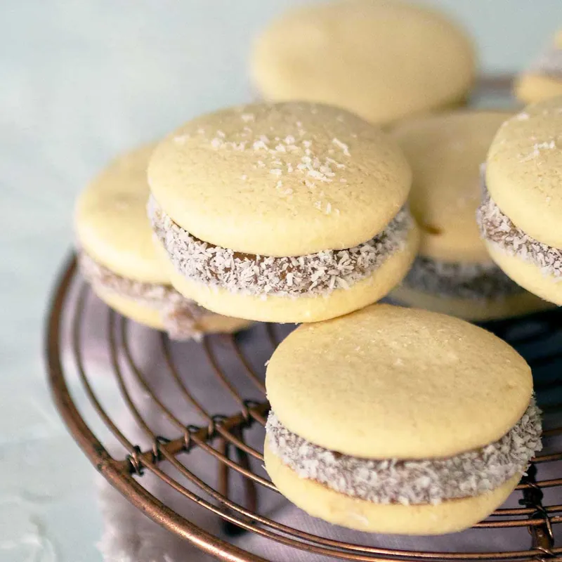 Pale round alfajores sandwich cookies filled with dulce de leche and rolled in finely shredded coconut