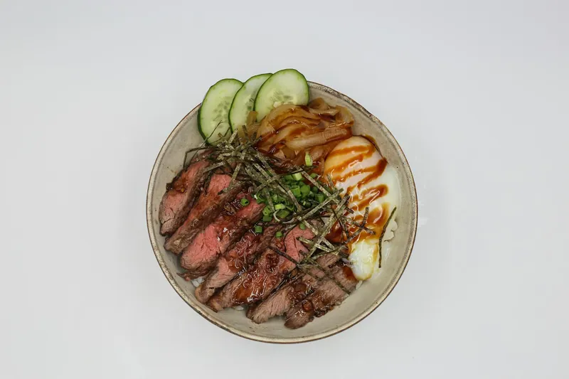 Sliced steak rice bowl with egg cucumber and scallions