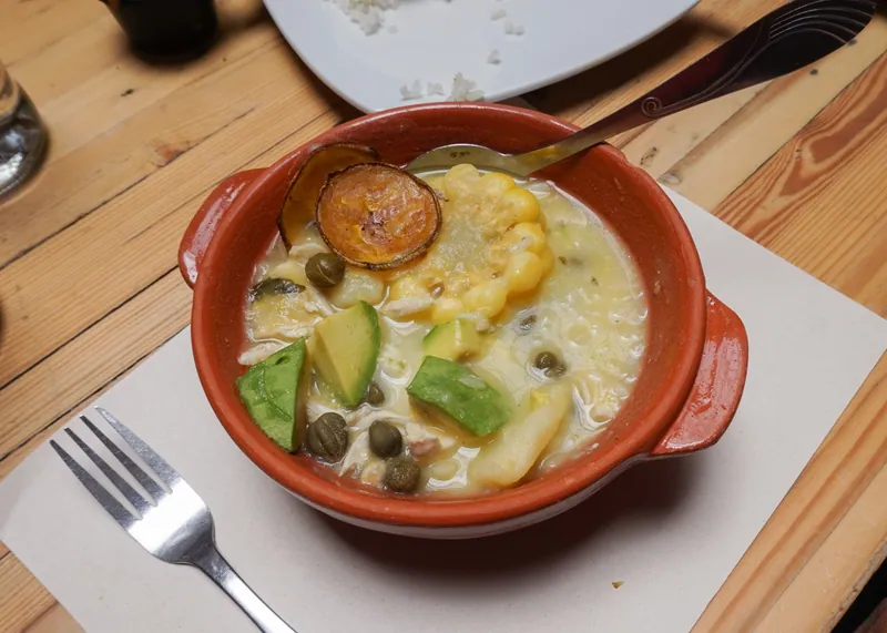 Clay bowl of Colombian-style ajiaco with creamy potato broth, corn, avocado, capers and chicken
