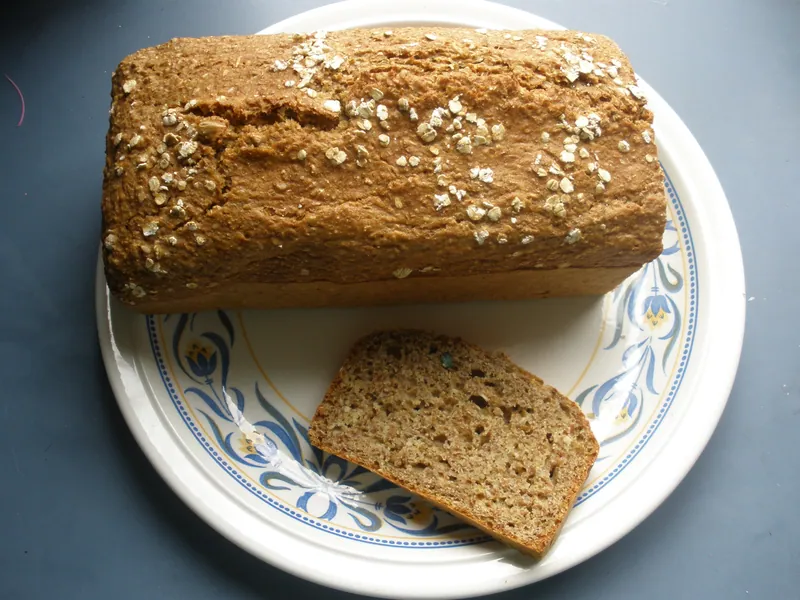 Oat-topped rectangular loaf of Irish brown soda bread with one slice showing its coarse whole-grain crumb