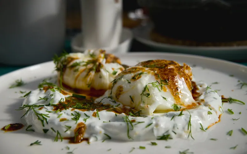 Two poached eggs on thick herbed yogurt with reddish Aleppo butter and fresh dill on a white plate