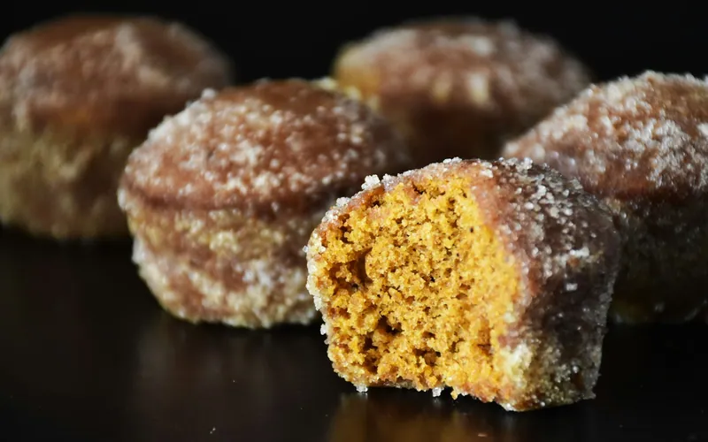 Small orange pumpkin muffins coated all over in sparkling cinnamon sugar, with one cut open to show the tender spiced crumb