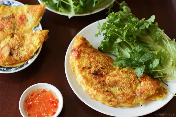 Two crisp golden Vietnamese bánh xèo folded into half-moons and served with lettuce, fresh herbs, vegetables and orange fish-sauce dip