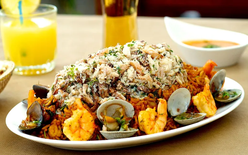 Saffron-red seafood paella rice piled with large shrimp, opened clams and mussels, generous white crab meat, chopped parsley, and lemon nearby