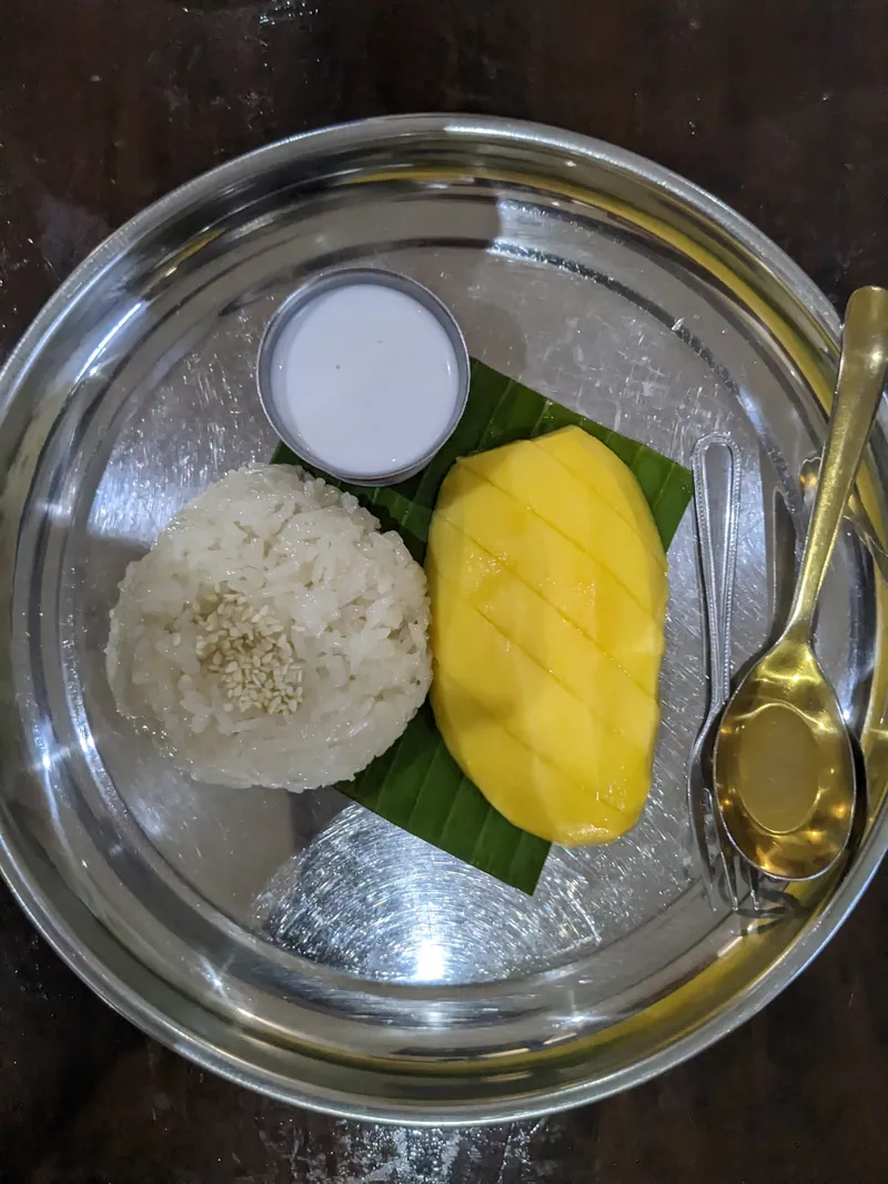 Thai mango sticky rice with sliced ripe mango, white coconut cream and sesame seeds on a banana leaf