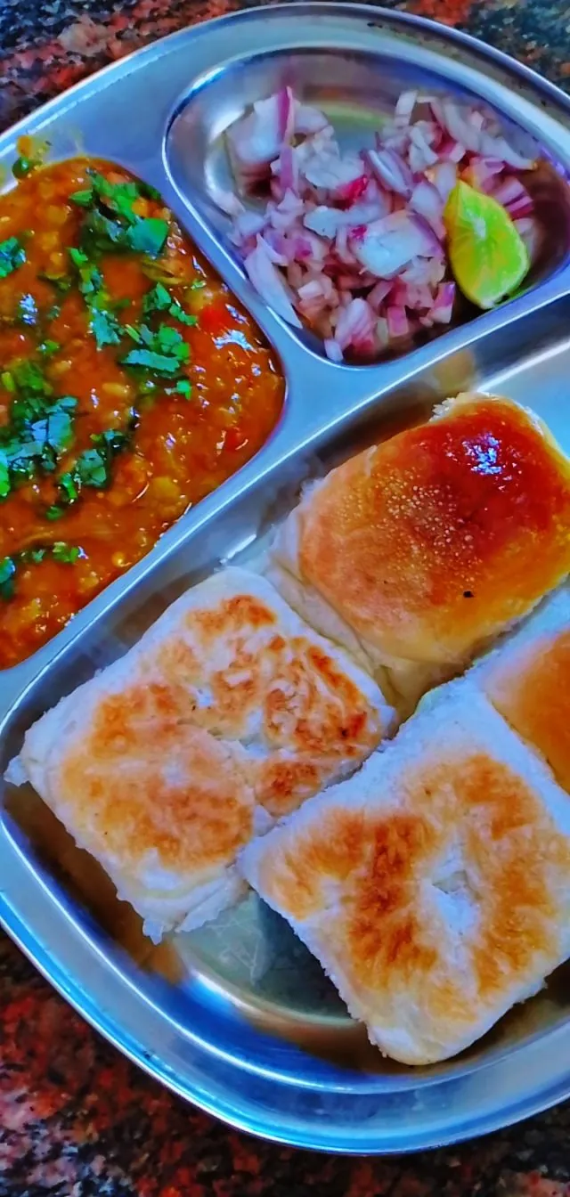 Mumbai-style pav bhaji vegetable mash with two buttered rolls, chopped onions, cilantro and lime