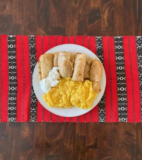 Romanian cabbage rolls filled with meat and rice beside yellow polenta and sour cream