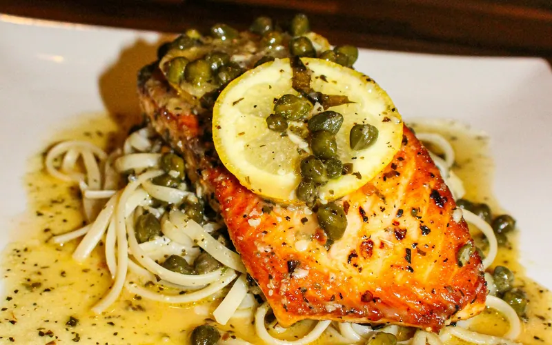 Golden seared salmon fillets over linguine with lemon slices, capers and a buttery herb-flecked pan sauce