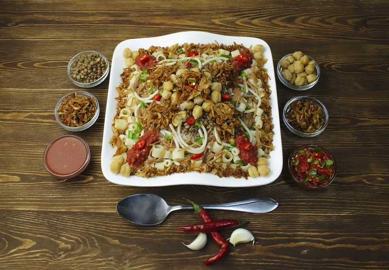 Egyptian koshari platter layered with rice, lentils, short pasta, chickpeas, tomato sauce, red chiles and abundant crispy onions