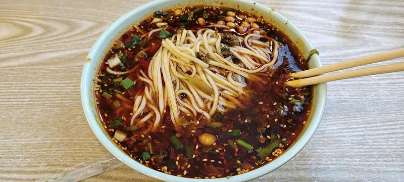 Soupy dan dan noodles in a red chile-sesame broth with crumbled pork, scallions, peanuts and sesame seeds
