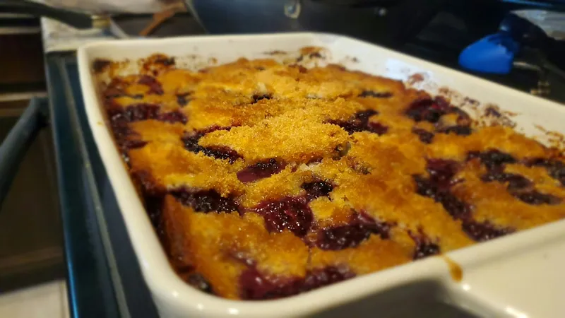 Blackberry and blueberry cornmeal cobbler in a white rectangular baking dish with a crisp golden sugar crust