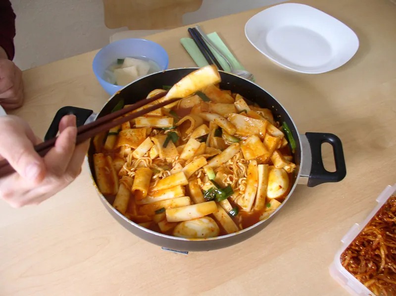 Glossy red Korean tteokbokki with cylindrical rice cakes, folded fish cakes, cabbage, carrots and scallions