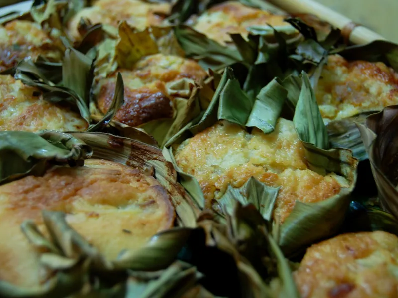 Individual golden Filipino bibingkang galapong rice cakes baked in folded banana leaves with coconut and cheese