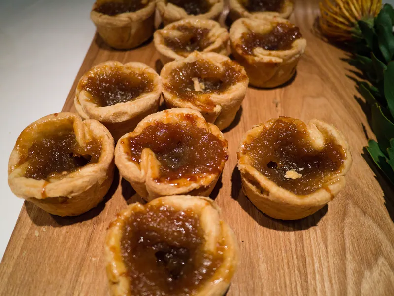 Nine rustic Canadian butter tarts with flaky golden pastry, glossy brown-sugar filling and visible raisins on a wooden board