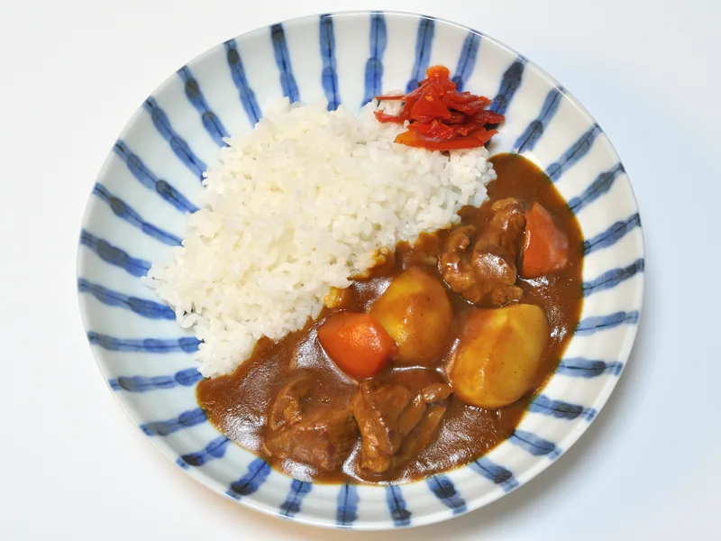 Japanese-style brown beef curry with whole potato and carrot pieces beside white rice and red pickles