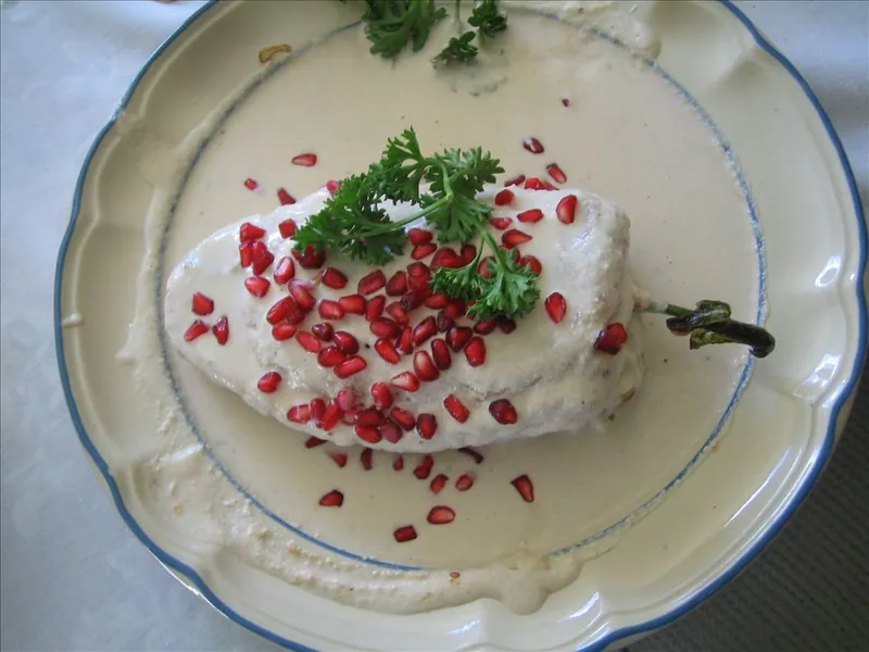 Roasted poblano stuffed with pork-fruit picadillo and covered in walnut cream, pomegranate seeds and parsley