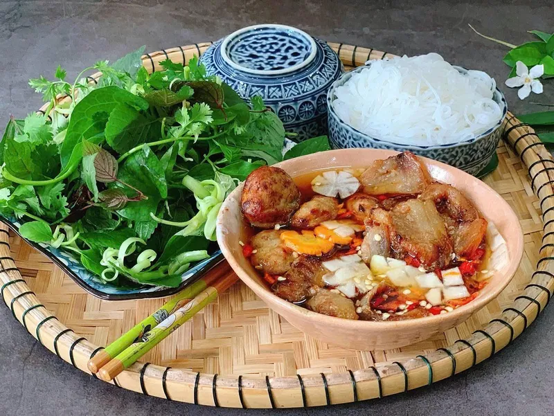 Hanoi bún chả with grilled pork patties and slices in dipping broth beside rice noodles and fresh herbs