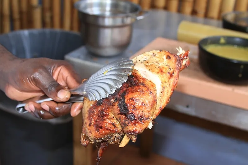 Whole Jamaican jerk chicken with deeply browned spice-coated skin being lifted from the grill with metal tongs