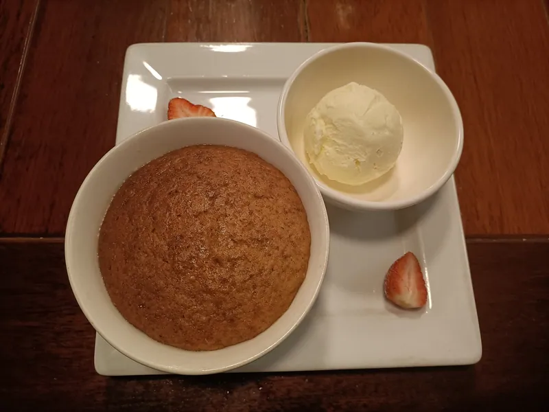 Individual round malva pudding with a glossy brown top served beside a scoop of vanilla ice cream and strawberry halves
