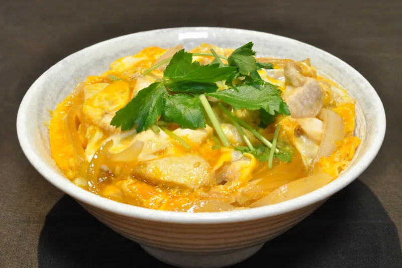 Japanese oyakodon bowl with pieces of chicken, softly set golden egg, translucent onion and mitsuba over steamed rice